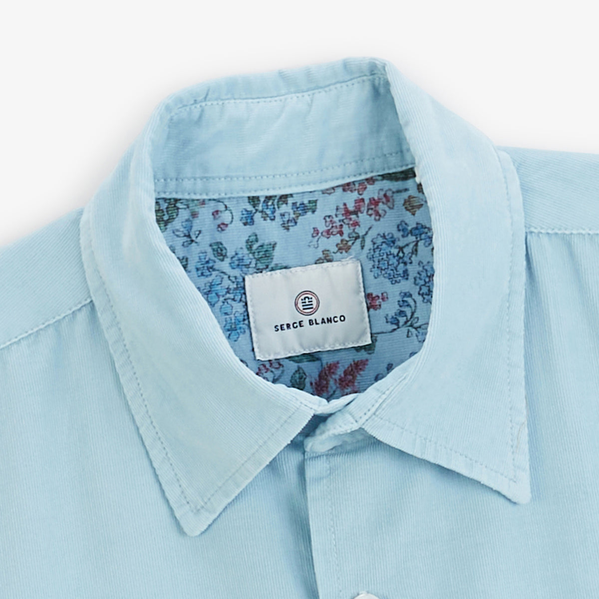 Détail du col et de la doublure intérieure à motif floral de la chemise en velours côtelé bleu.