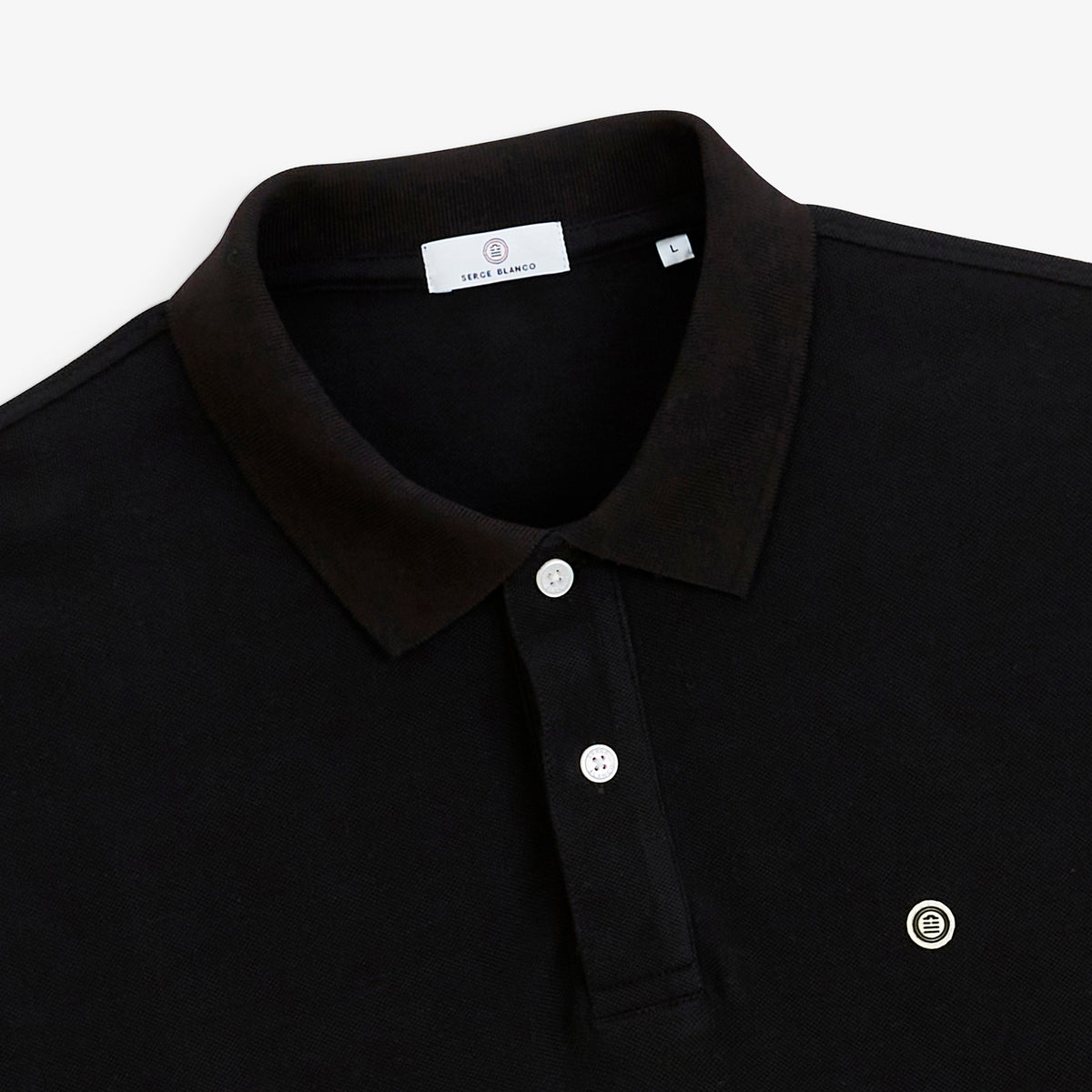 Détail du col, des deux boutons blancs et du logo poitrine du polo piqué Lucas noir SERGE BLANCO.