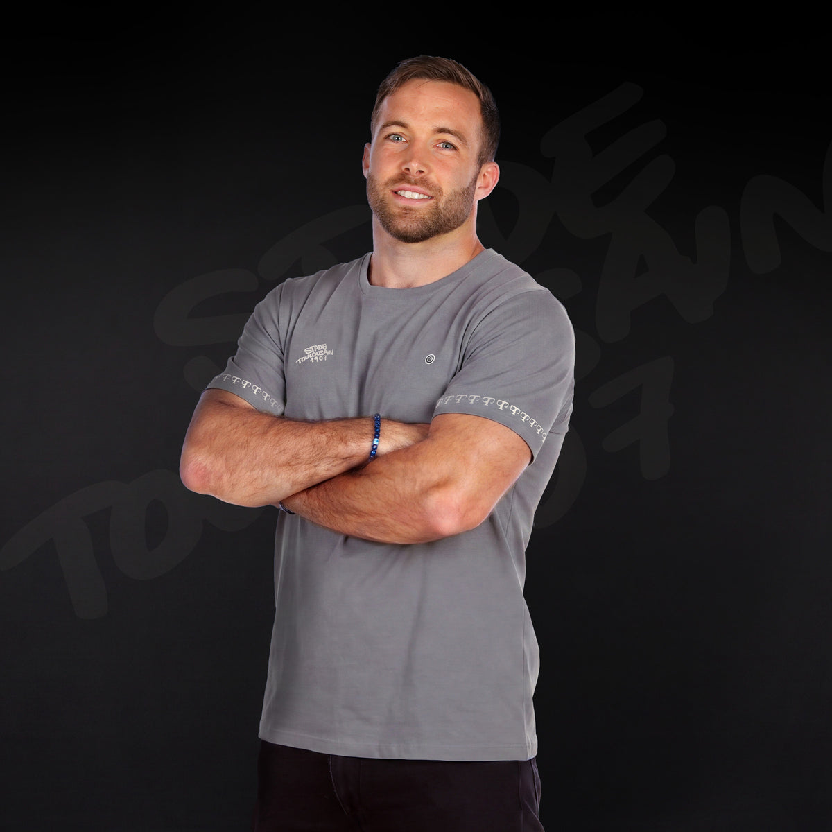Graues T-Shirt „1907“ mit dem Monogramm des Stade Toulousain, von einem Model mit verschränkten Armen von vorne getragen.