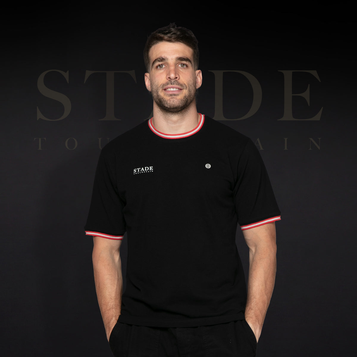Maglietta “Stade” nera dello Stade Toulousain indossata di fronte da un modello, con bordini rossi e bianchi sul colletto e sulle maniche.