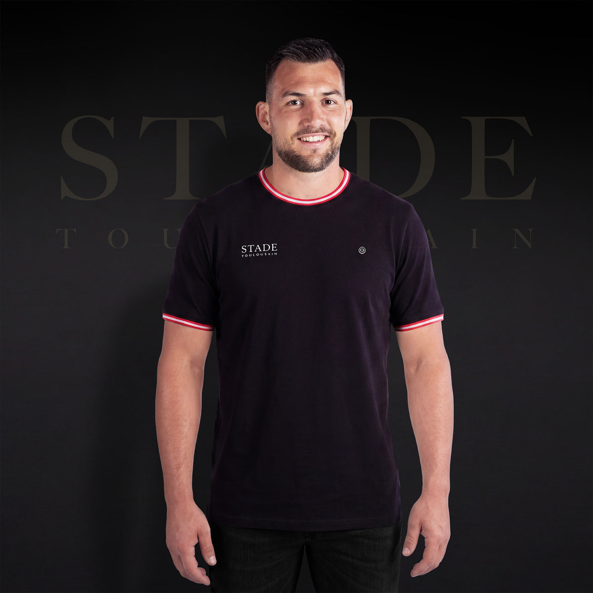 Maglietta “Stade” nera dello Stade Toulousain indossata di fronte da un modello, con logo sul petto e bordature rosse e bianche.